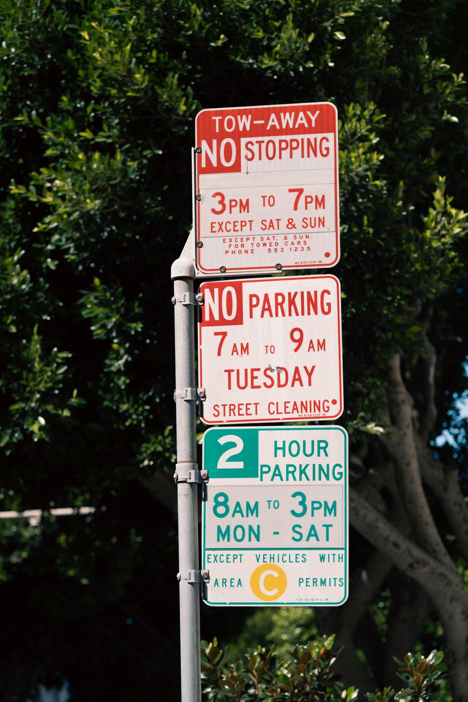 Street parking signs displaying timing and rules in a shaded urban area.