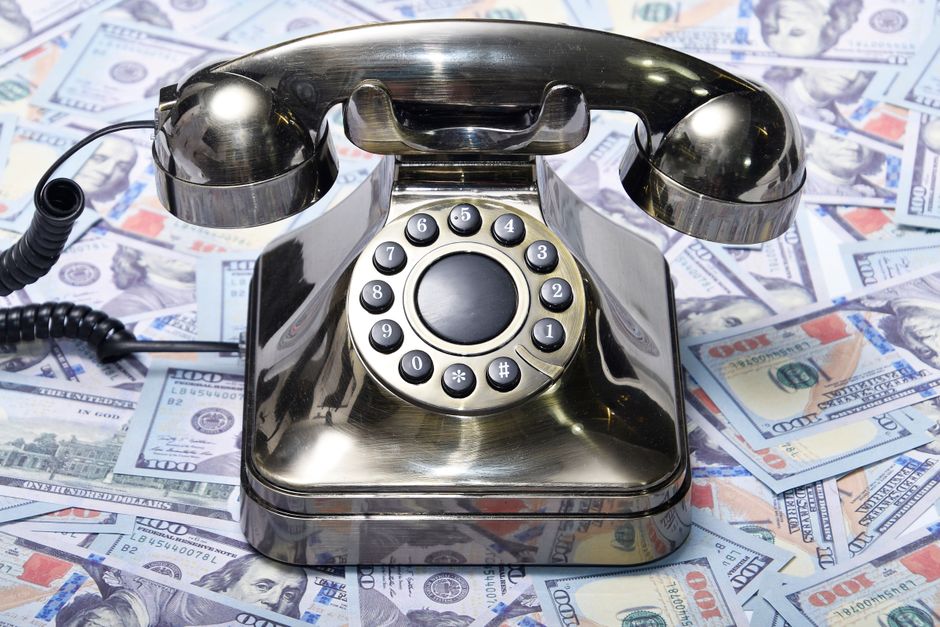 A retro rotary phone placed on a pile of US dollar bills, symbolizing communication and finance.