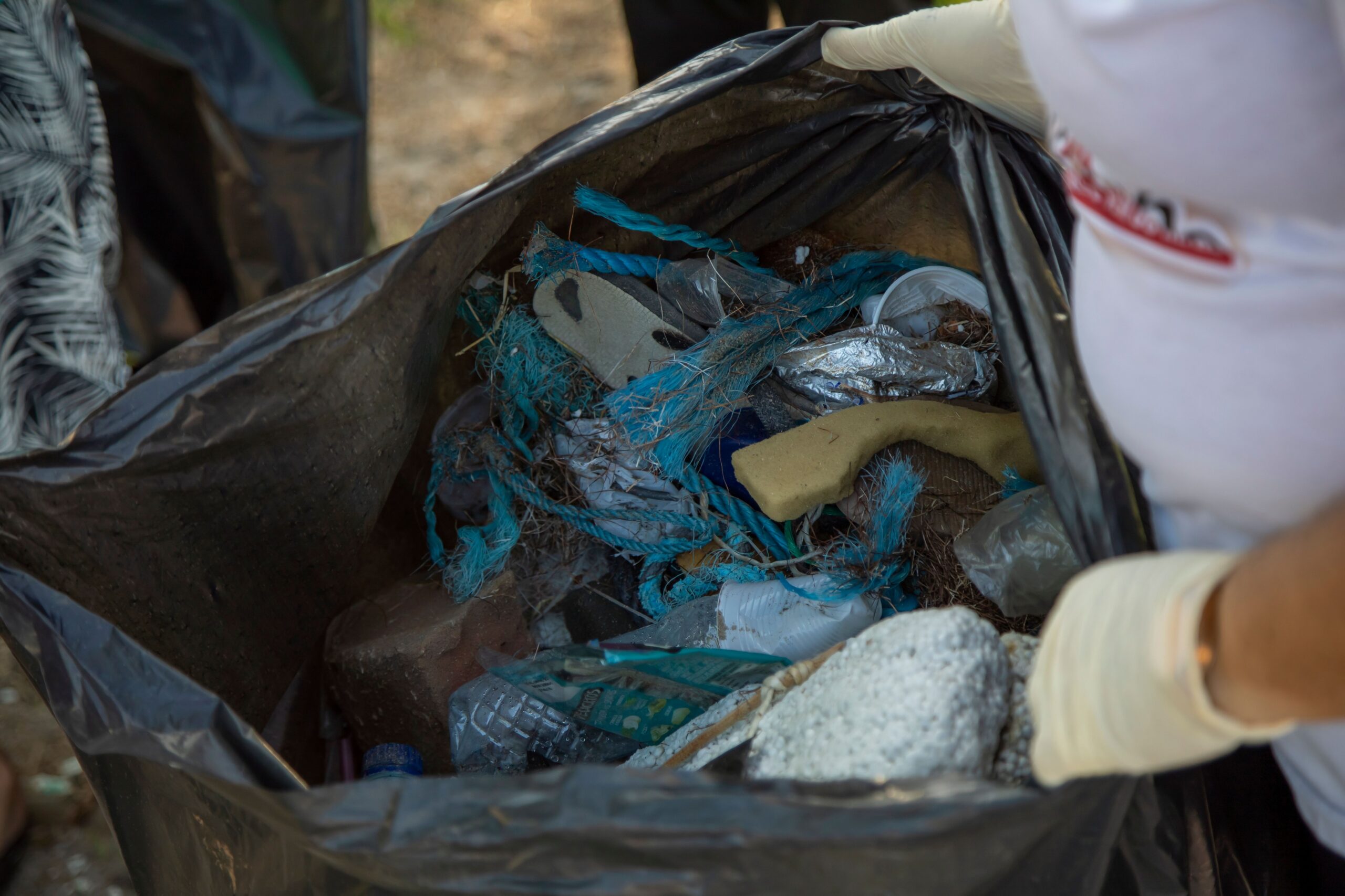 A close-up shot of a black trash bag filled with assorted garbage, including plastic waste.