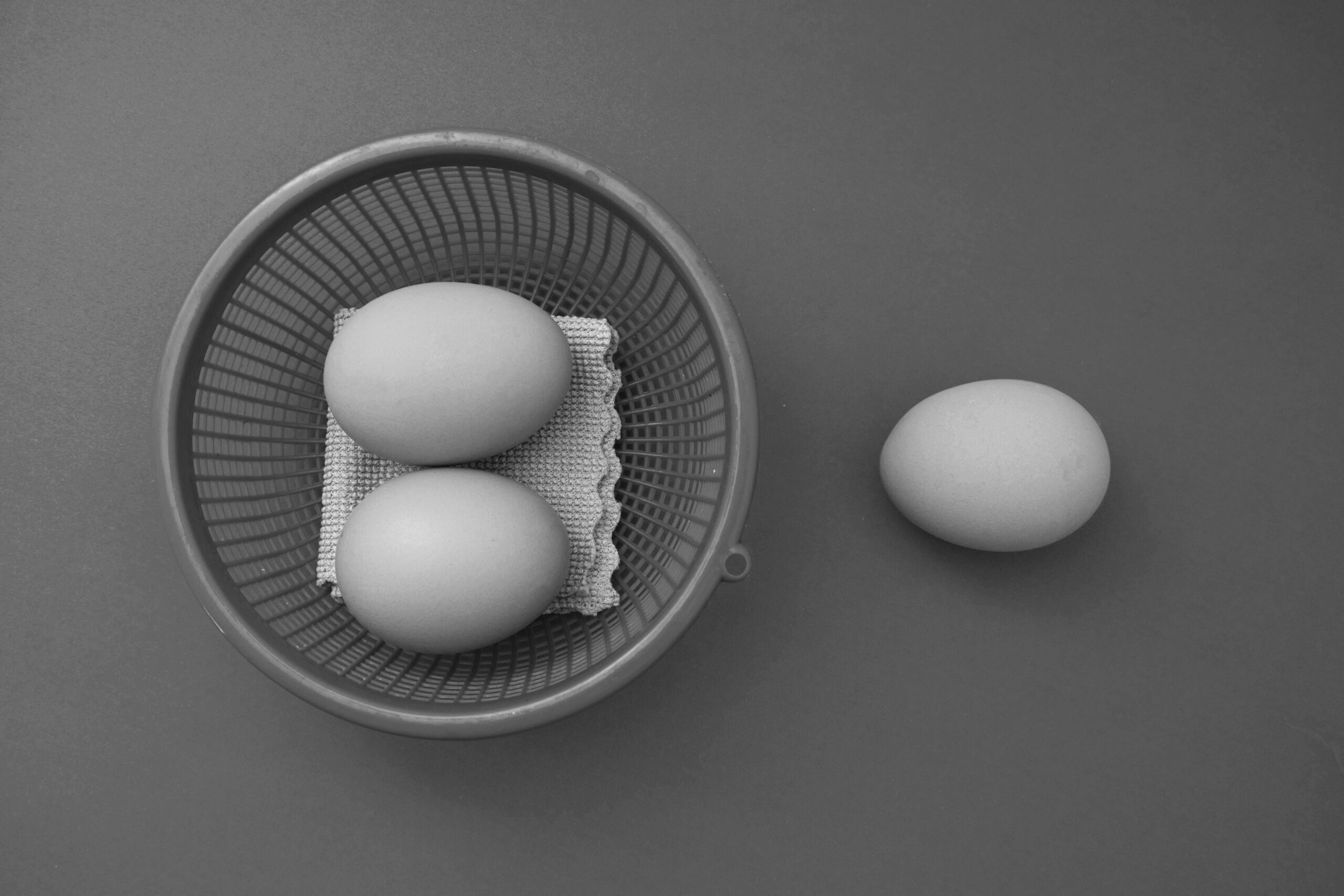 Monochrome image of three eggs with a basket on a gray surface, featuring a minimalist style.