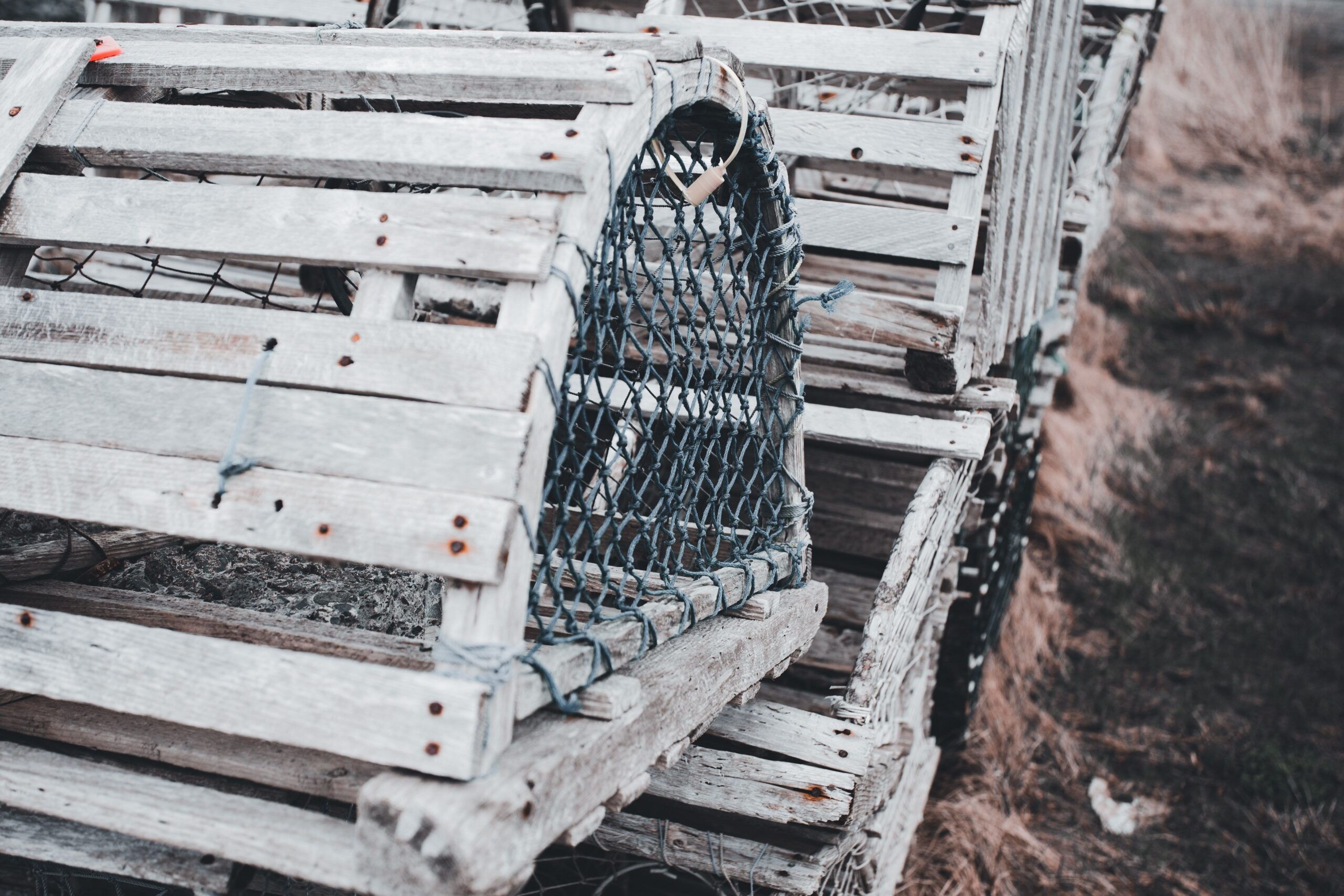 Close-up of weathered wooden lobster traps stacked along a shore, showcasing fishing industry tools.