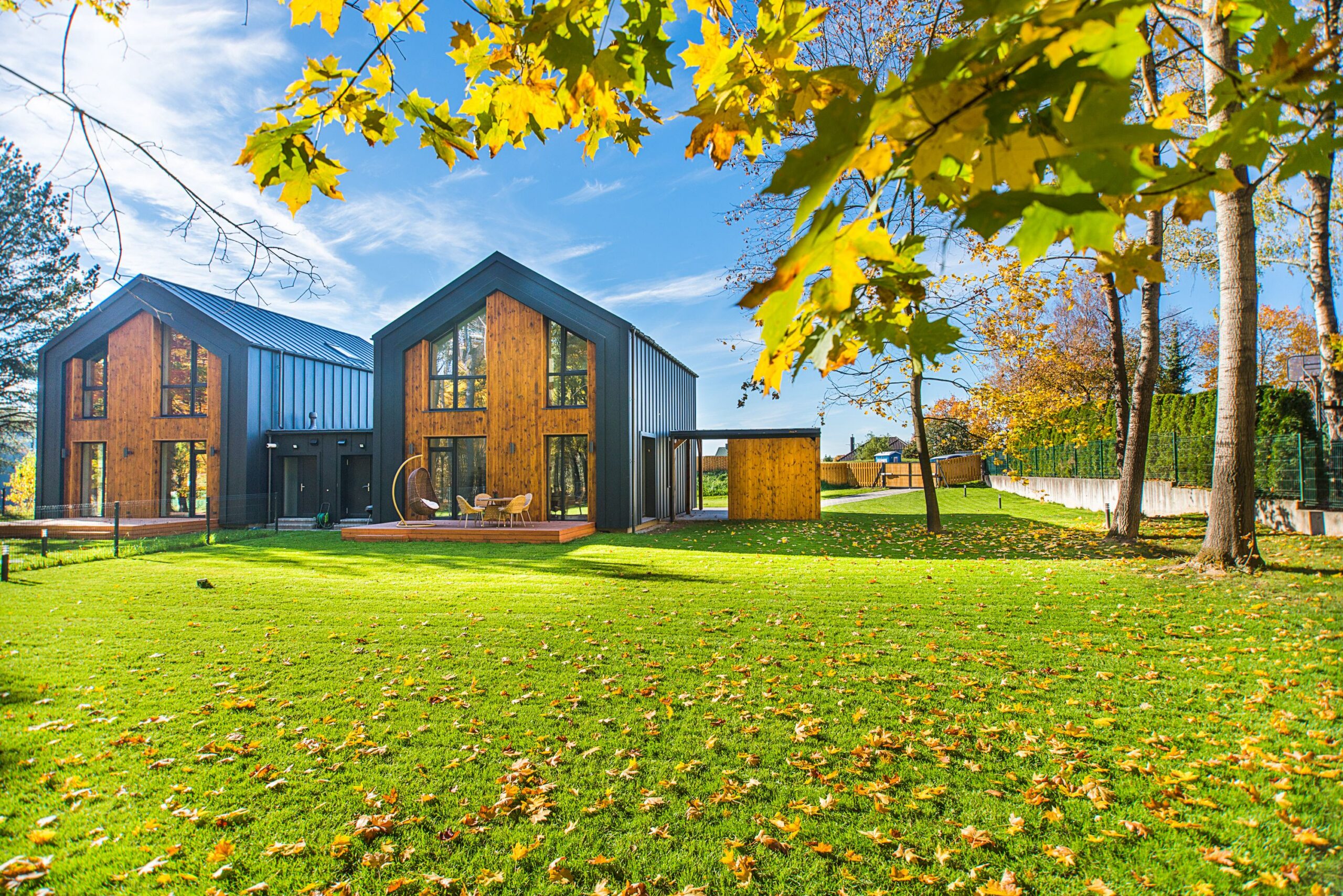 Contemporary wooden houses with lush green lawns surrounded by vibrant autumn foliage.