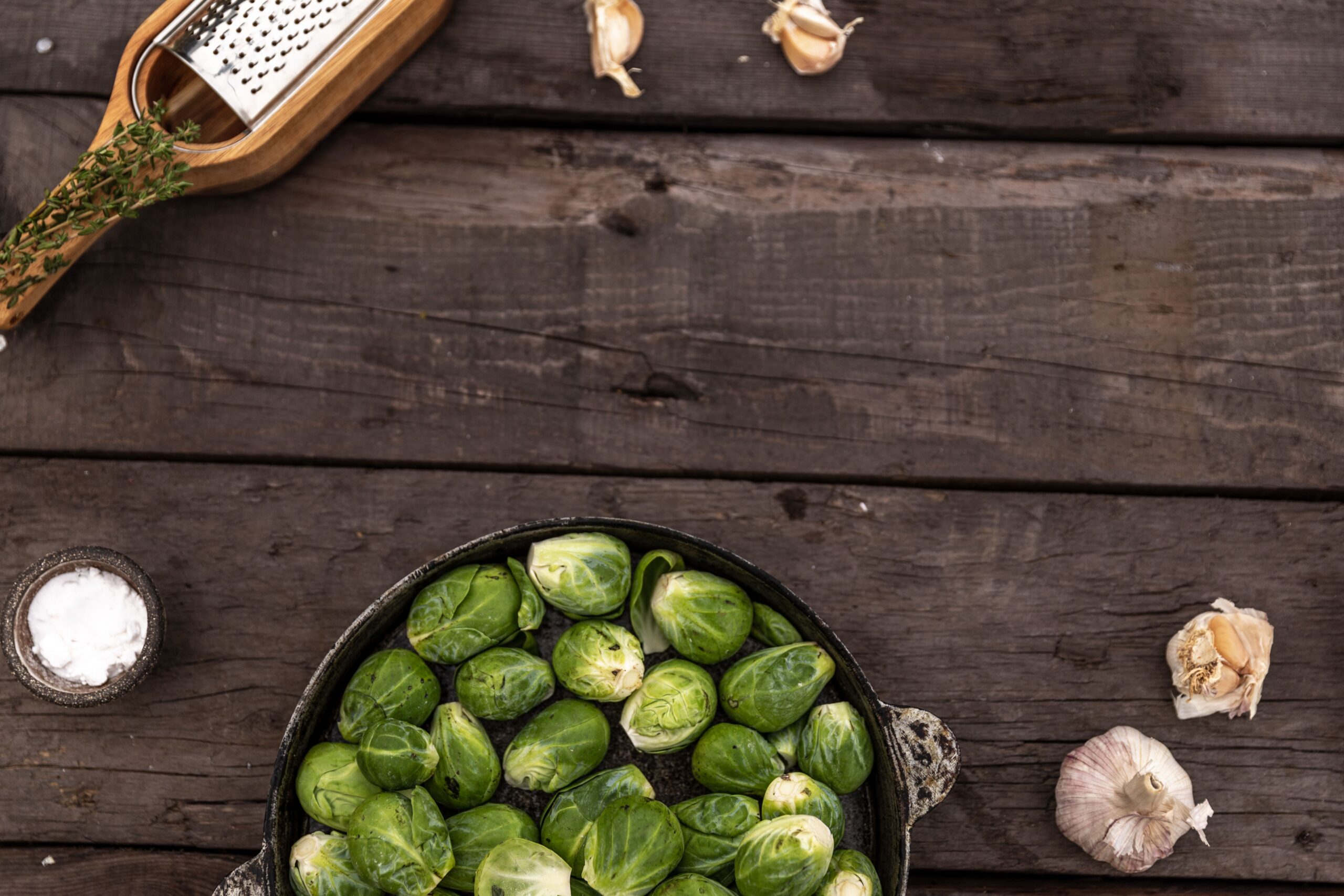 Top view of fresh Brussels sprouts with garlic on a rustic wooden surface, styled in a flatlay format.