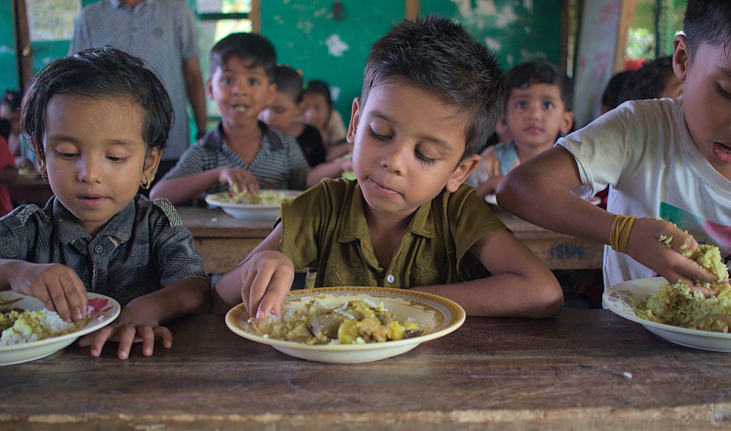 Young children eating lunch together in a classroom, sharing food.