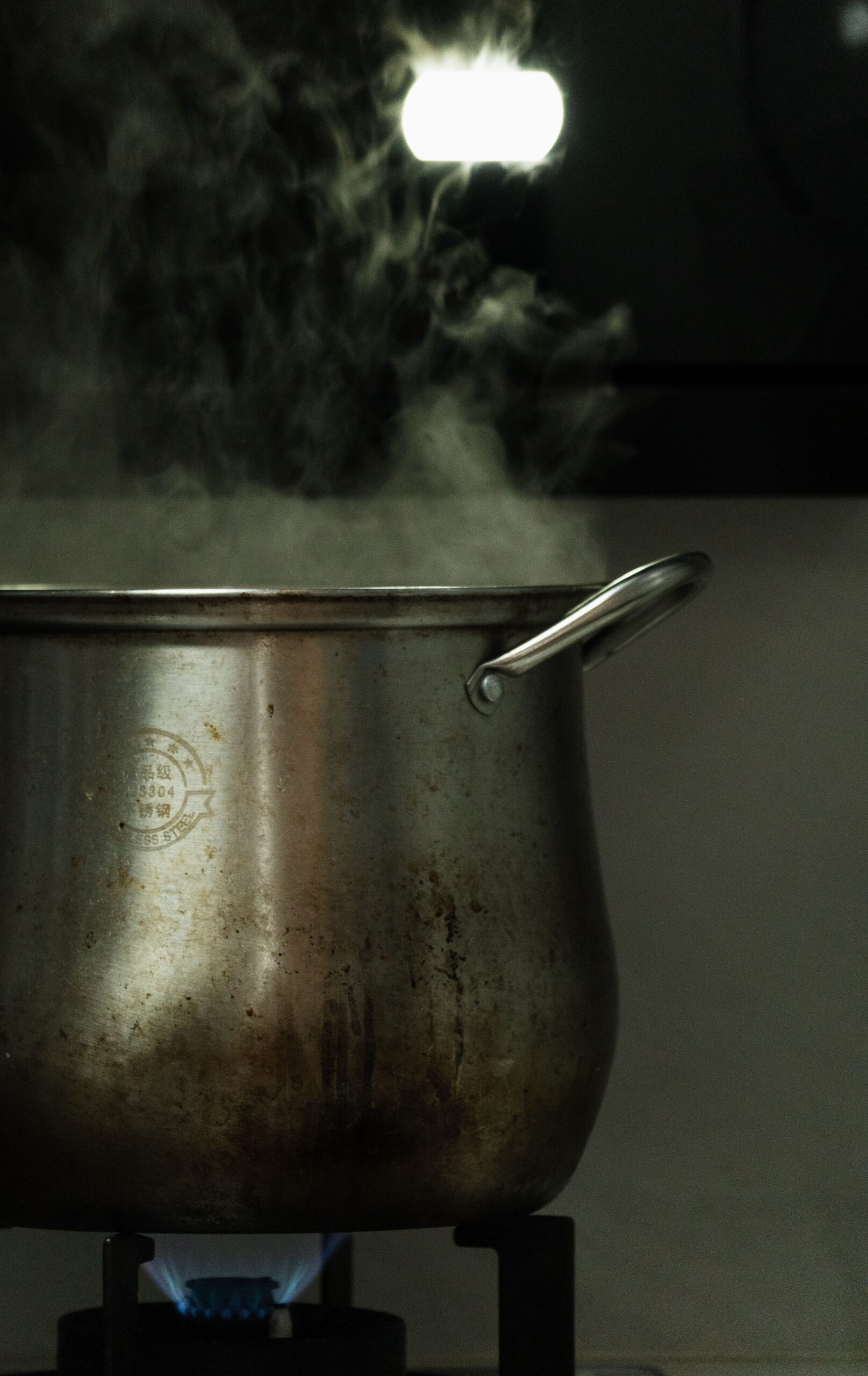 A stainless steel pot releasing steam while boiling on a gas stove indoors.