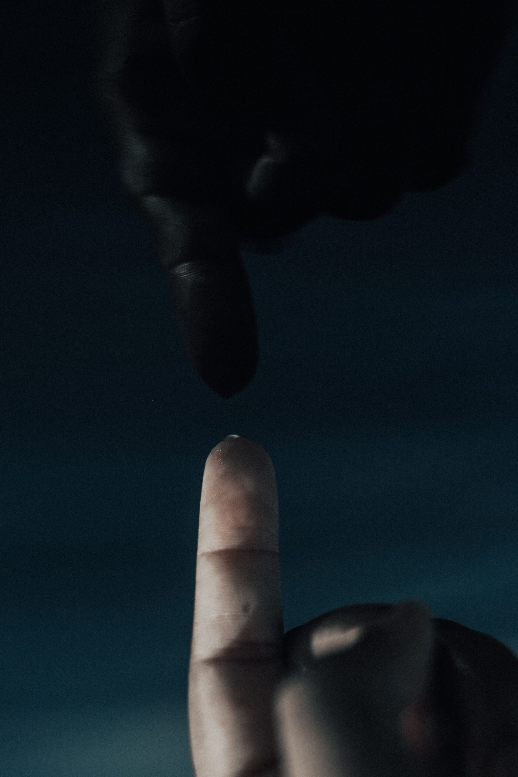 Dramatic close-up of two fingers almost touching with dark backdrop, conveying tension and anticipation.