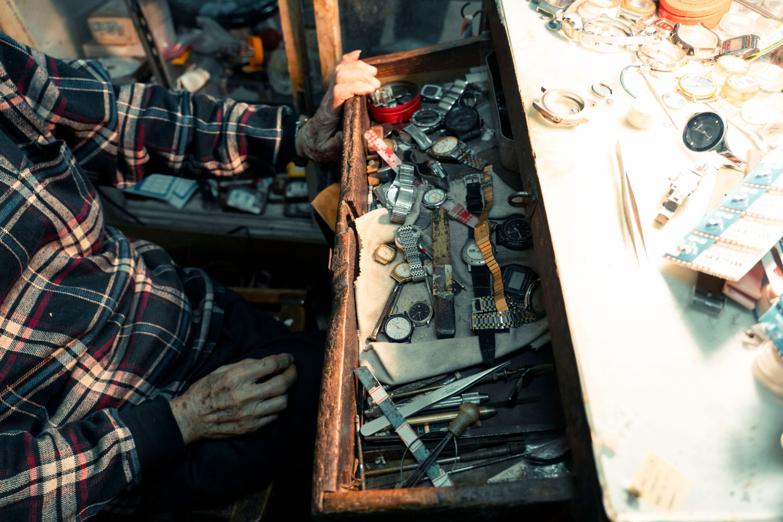 An artisan's hand at a workshop opens a drawer filled with watches, showcasing detailed repair tools.