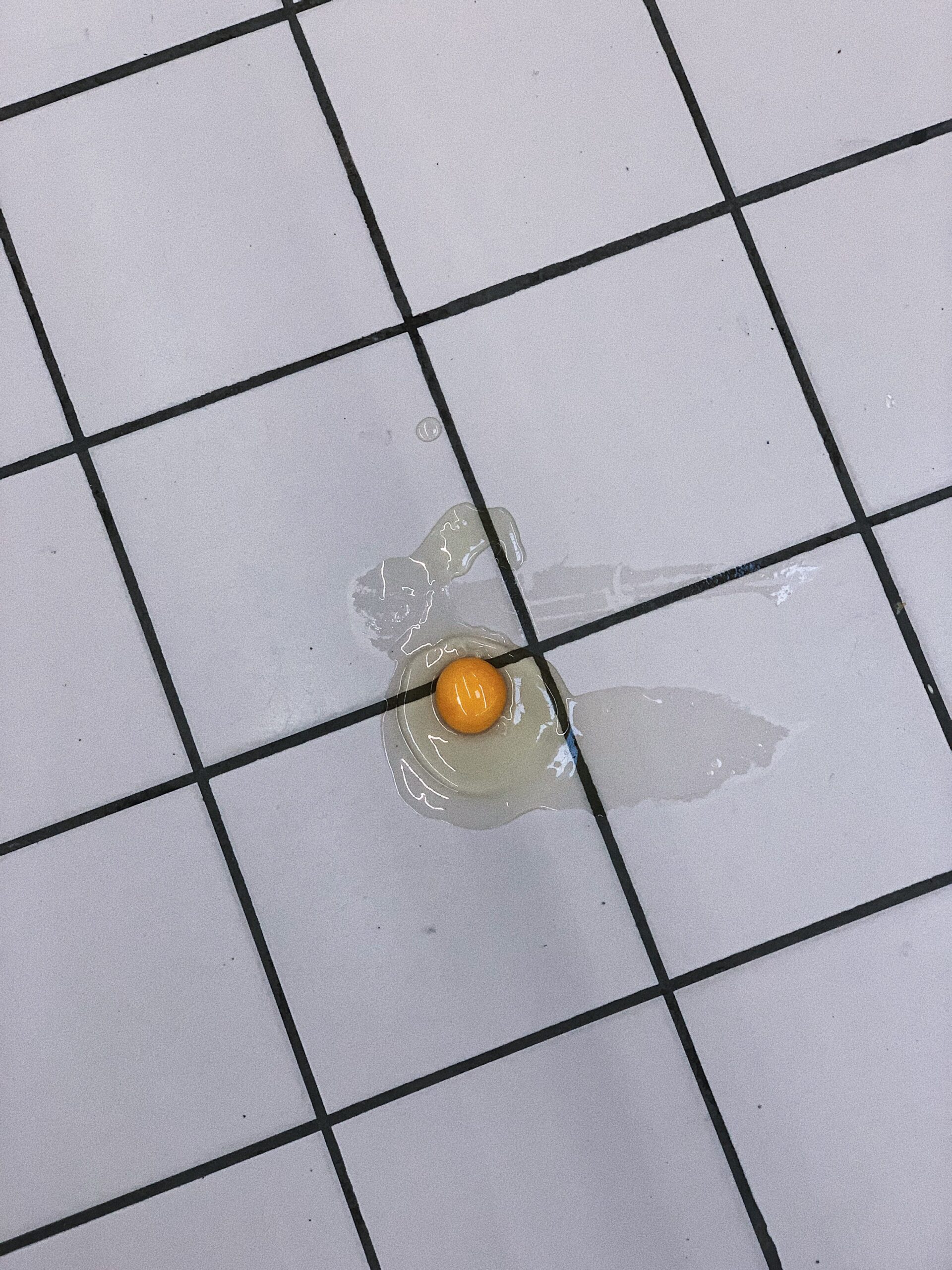 From above cracked uncooked egg without eggshell dropped on piled floor in kitchen