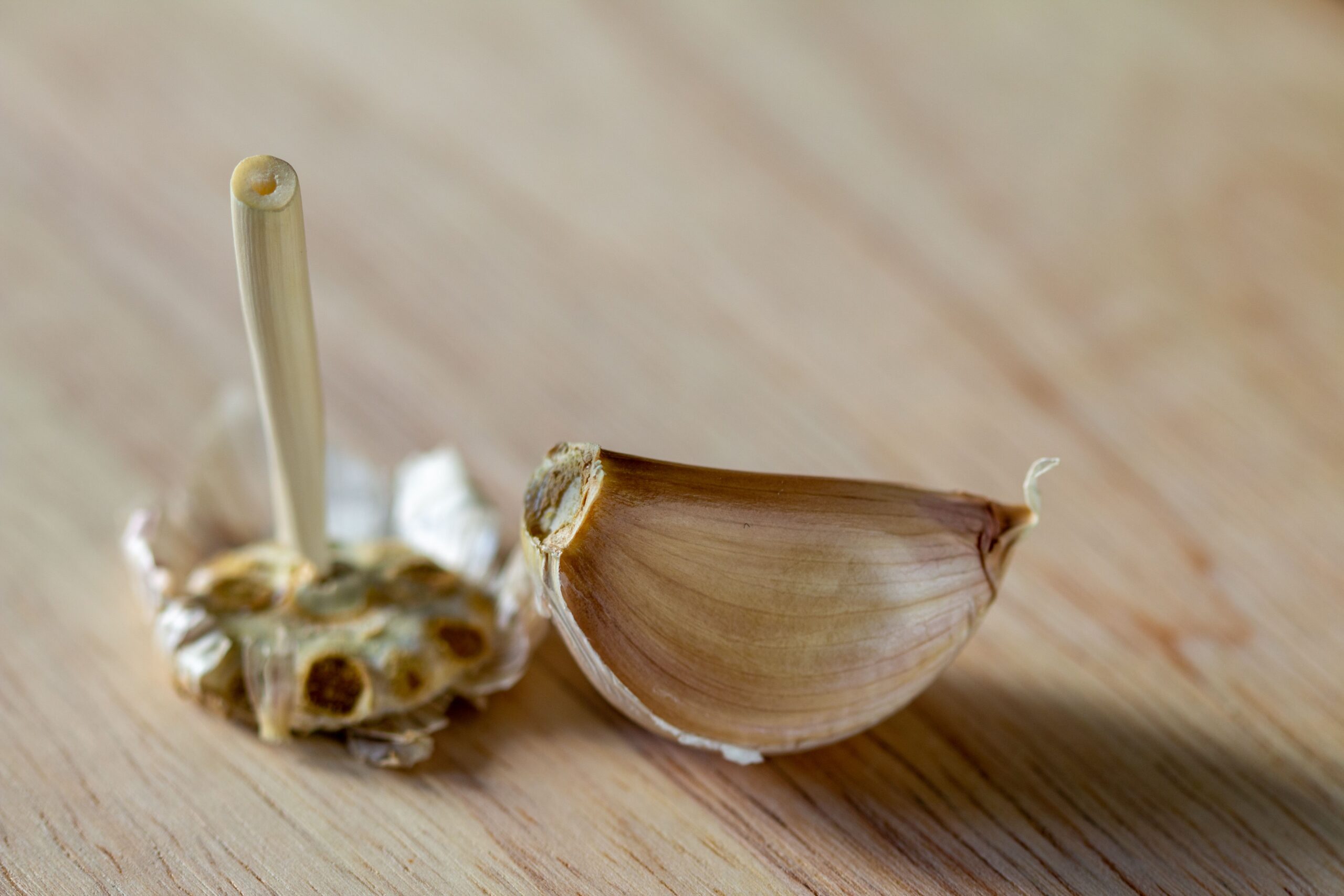 Macro shot of a single garlic clove with a peel on a wooden surface.