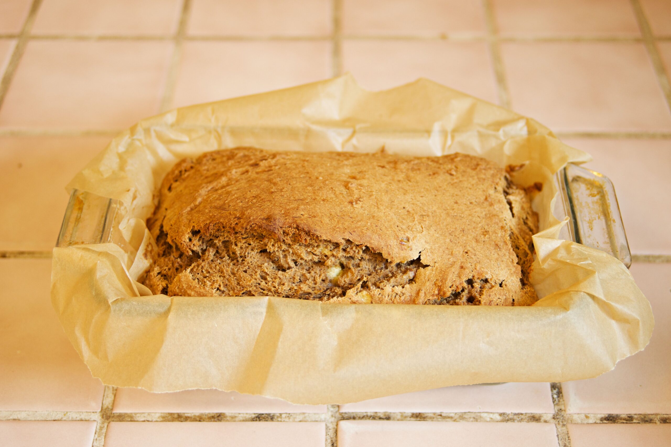 Delicious homemade banana bread fresh out of the oven in a parchment-lined glass pan.