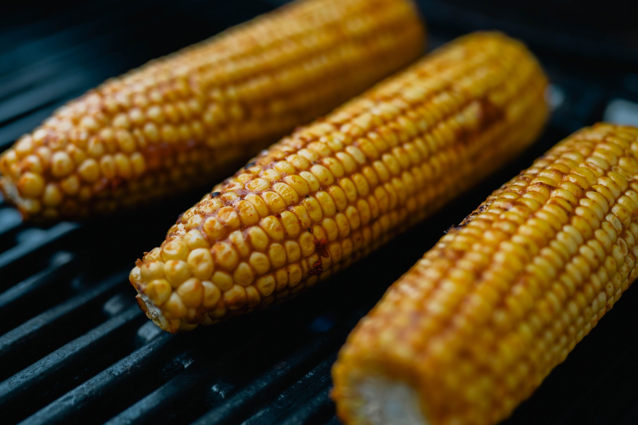Close-up of sizzling grilled corn on the cob, showcasing charred texture on a barbecue grill.
