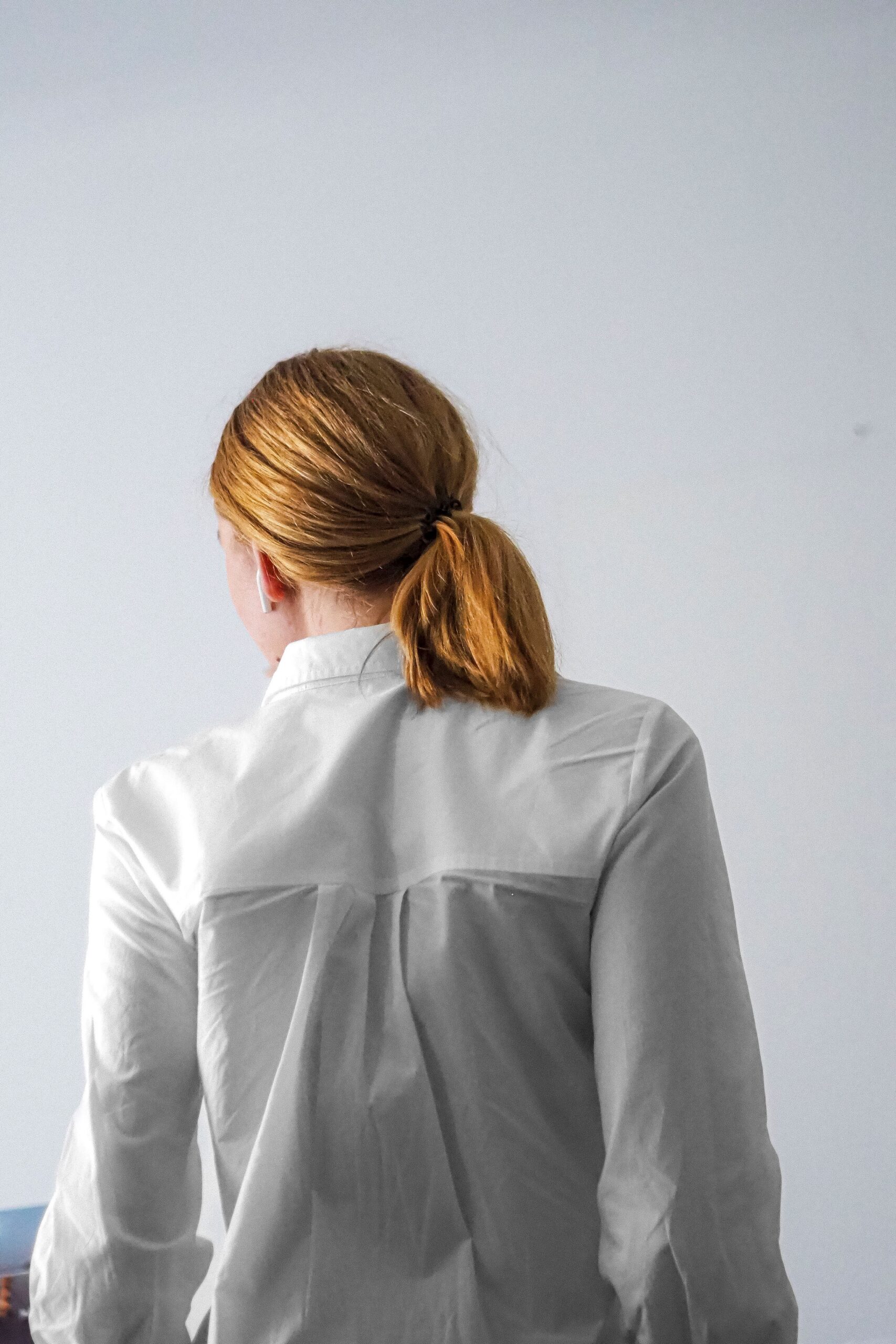 A person with a white shirt seen from behind against a minimalist background, suggesting solitude.