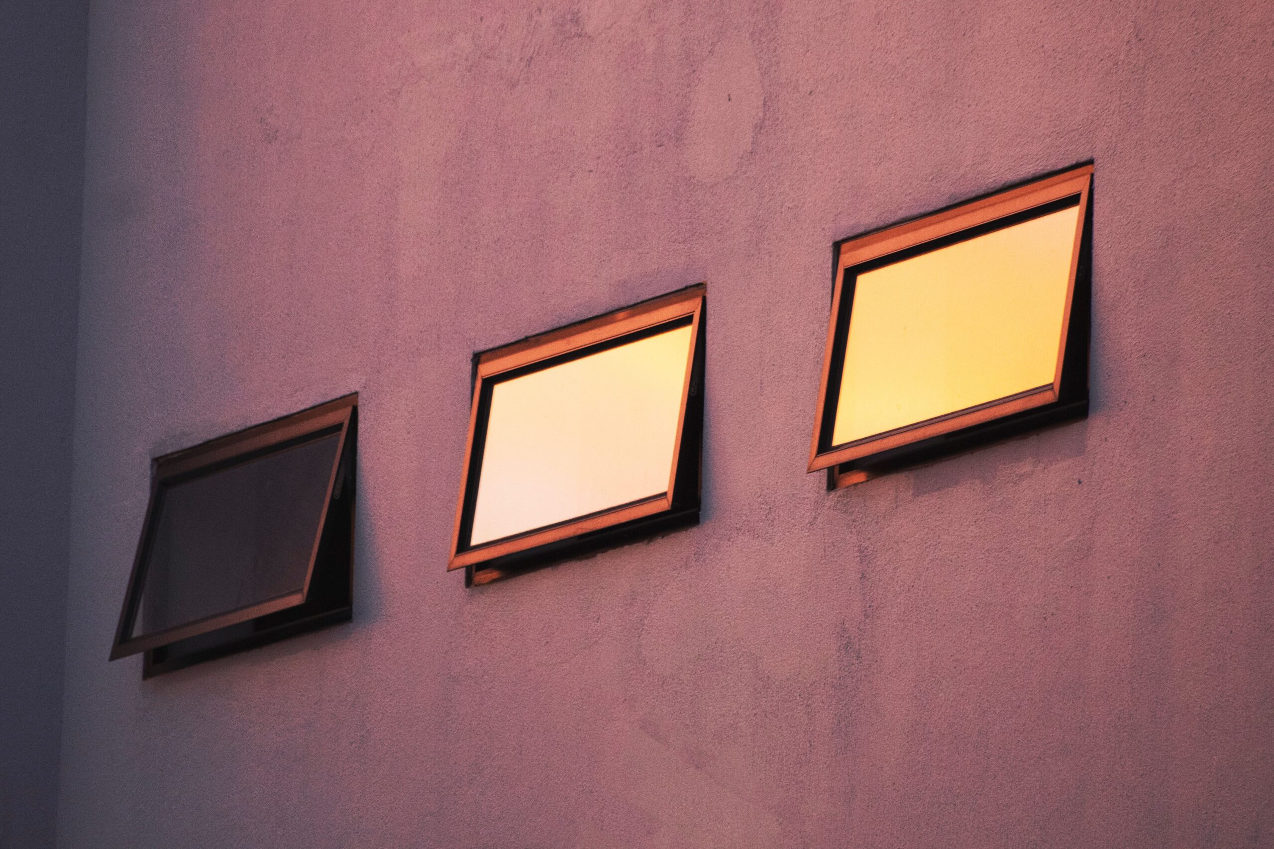 Three windows reflecting sunlight on a minimalist concrete wall during sunset.