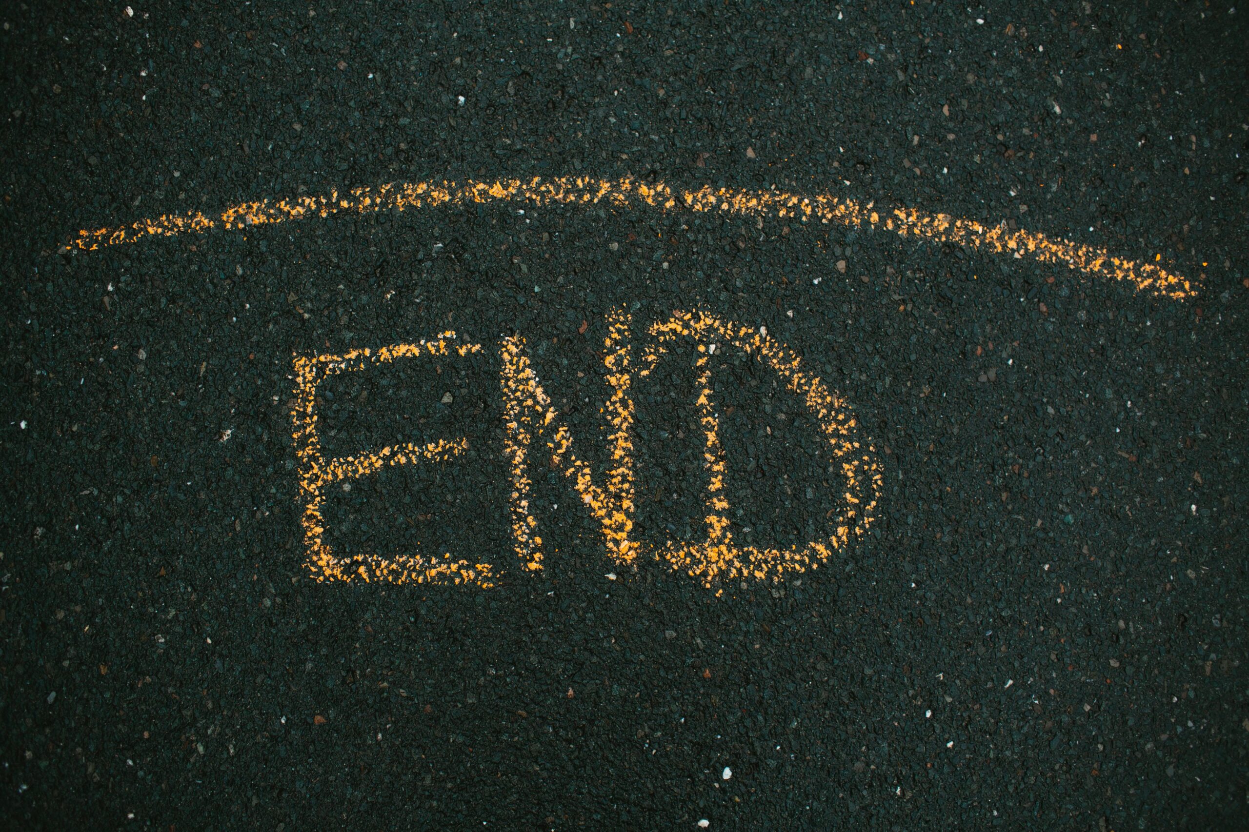 Close-up of 'END' written on asphalt with yellow chalk.
