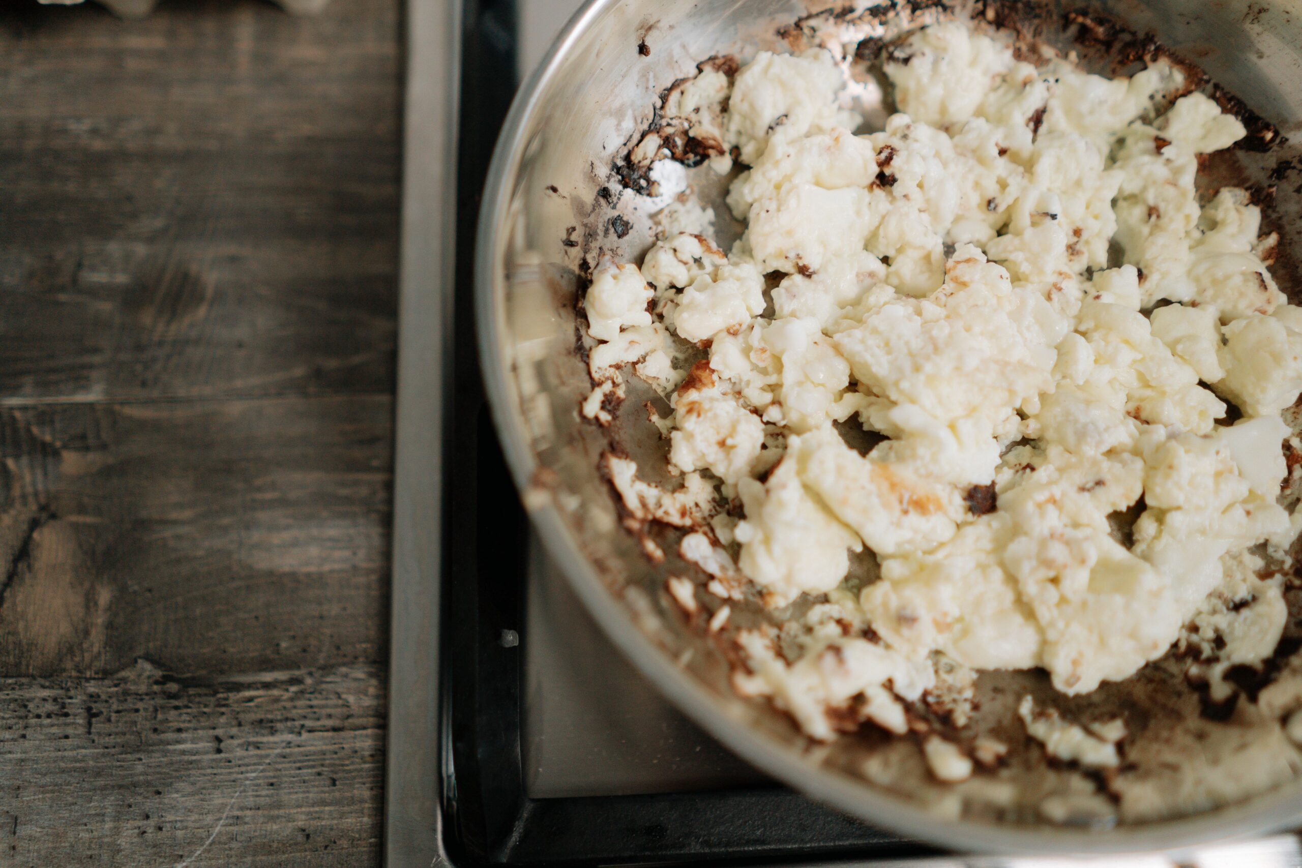 Overcooked scrambled eggs in a stainless steel skillet on a stove.
